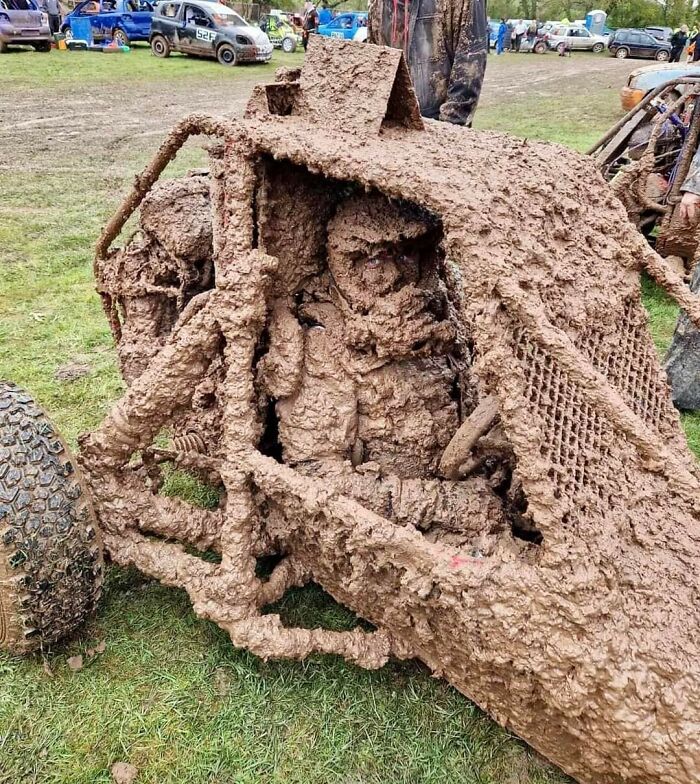Mud-covered vehicle with driver inside at a muddy field event, capturing a 'Hmmm' moment.