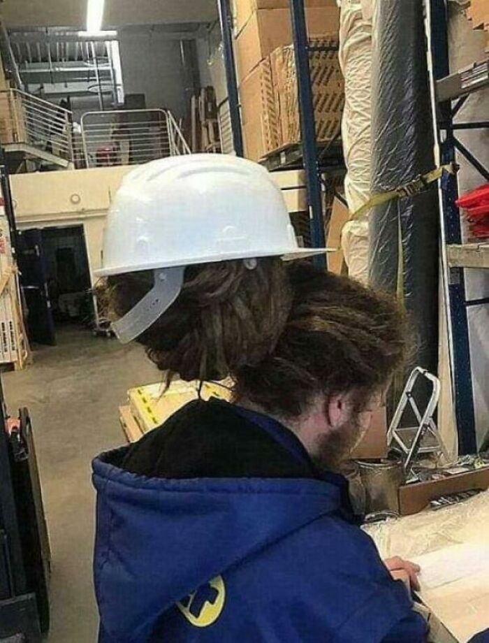 Person with a unique hard hat fit due to hairstyle in a warehouse, creating a 'hmmm' moment.