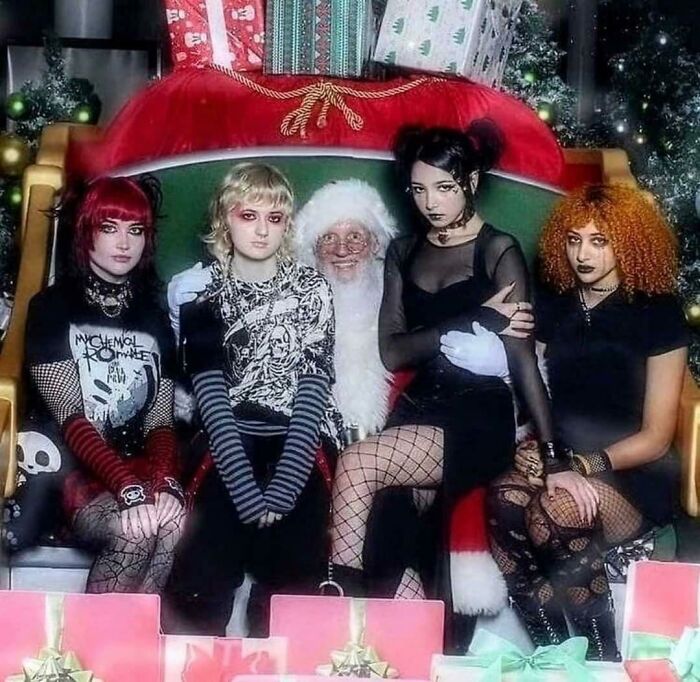 Santa with four goths on Christmas-themed chair surrounded by gifts, an unexpected 'Hmmm' moment.