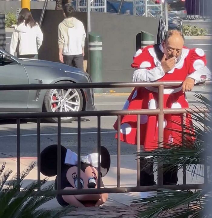 Man in polka dot dress, holding Minnie Mouse head, making people go "hmmm" on a city street.