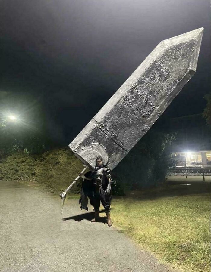 A person dressed in a costume holds an enormous sword at night, evoking curiosity.