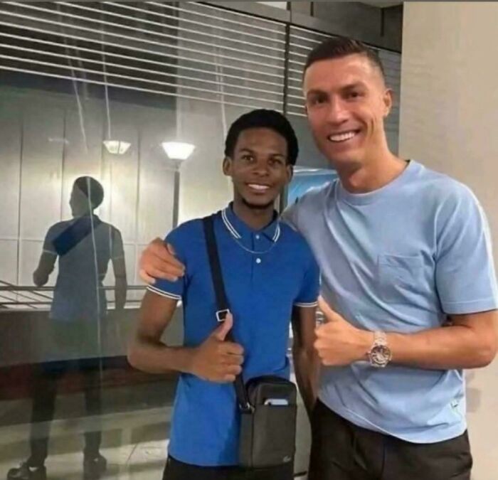 Two people smiling and posing with thumbs up in front of a reflective surface, creating a curious visual effect.